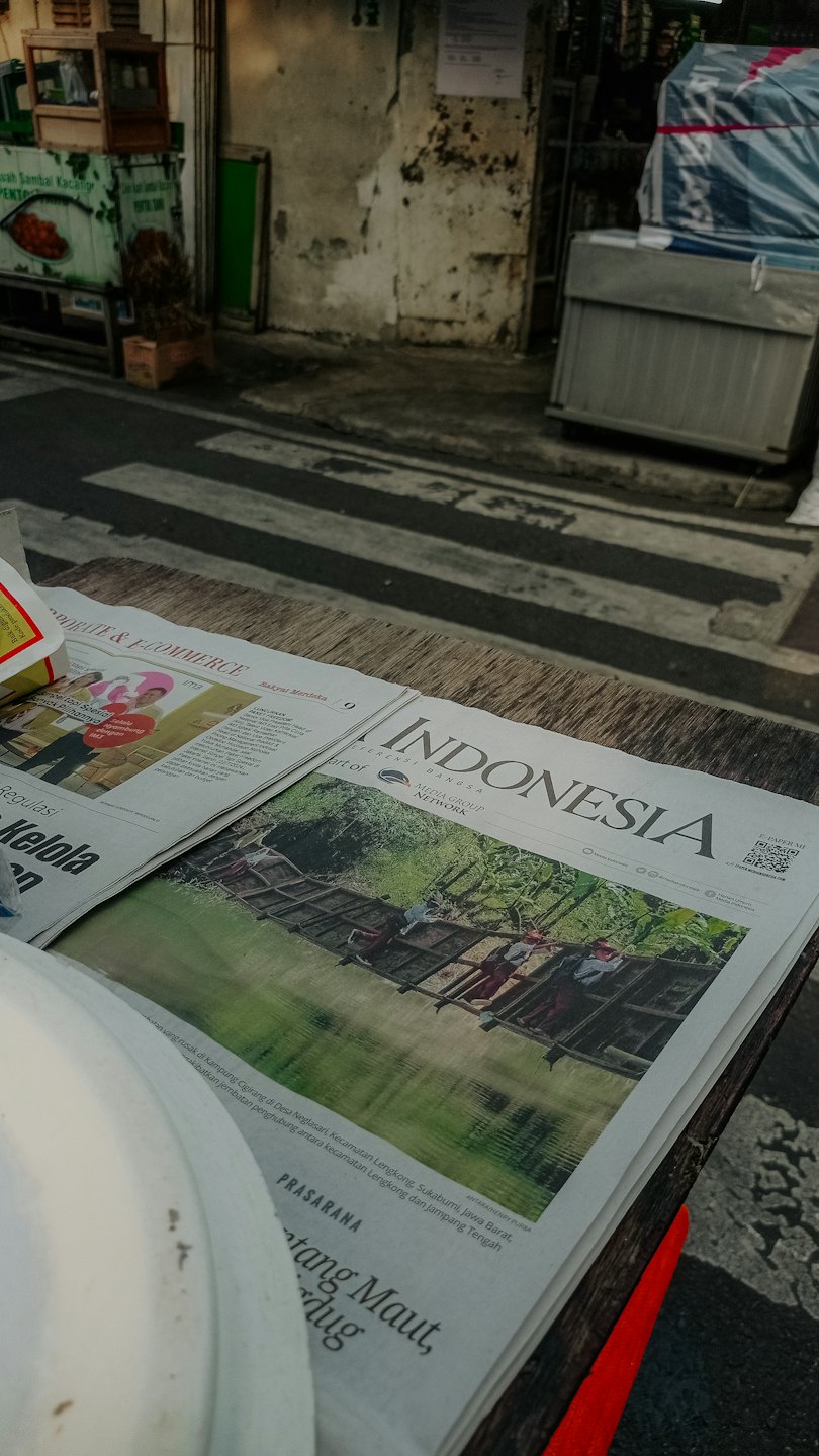 Giornale aperto su un tavolo di legno con sfondo urbano.