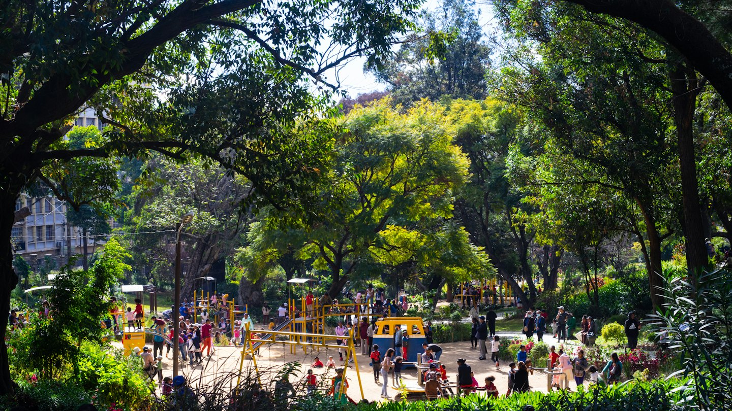 Persone che giocano su attrezzature in un parco pubblico affollato.